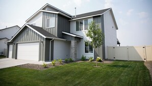 A modern two-story house with a garage, a small front yard with a tree, and a clear sky. - Meridian Sunset views w/playroom and private HOT TUB (Meridian)