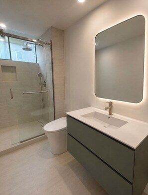 A modern bathroom with a glass-enclosed shower, a white sink with a large mirror, and a toilet. - Luxury 5-bedroom house with AC in Marina del Rey (Marina del Rey)