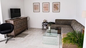 A modern living room with a sofa, a TV on a wooden cabinet, a black chair, a small side table with a vase, and three framed artworks on the wall. - New modern apartment, 74sqm, balcony, king-size box-spring bed (Offenburg)