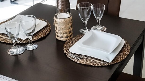 A dining table set with clear glasses, a white plate, and a woven placemat. - New modern apartment, 74sqm, balcony, king-size box-spring bed (Offenburg)