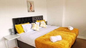 A double bed with a black headboard, a white nightstand, and a yellow throw blanket. - Home In Northampton | Contractors Welcome (Northampton)