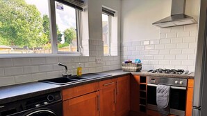 A compact kitchen with a washing machine, a gas stove, and wooden cabinets. - Home In Northampton | Contractors Welcome (Northampton)