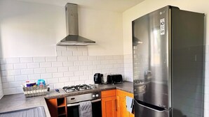 A compact kitchen with a stainless steel refrigerator, a gas stove, a toaster, and wooden cabinets. - Home In Northampton | Contractors Welcome (Northampton)