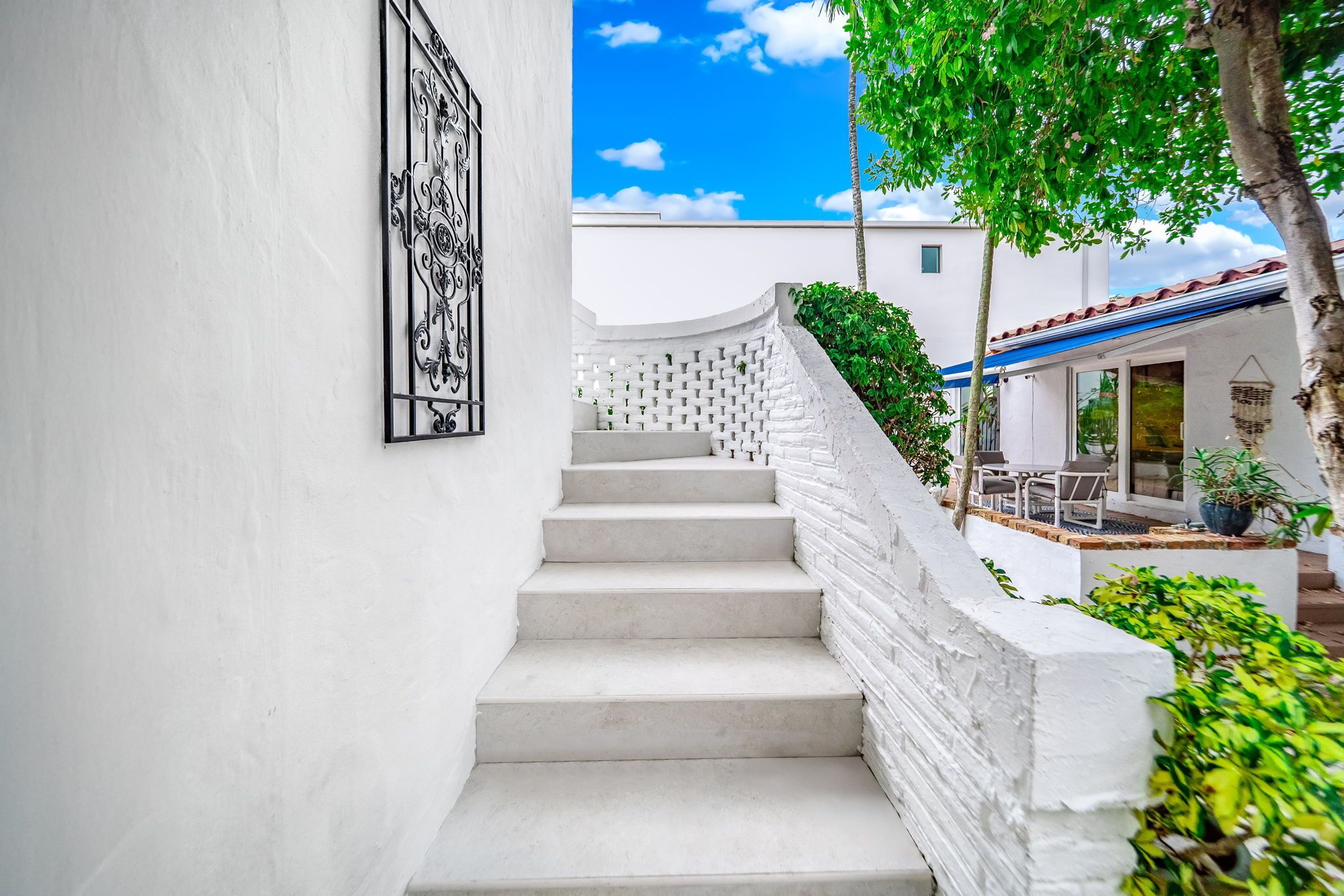A white staircase leading to a house with a blue roof, surrounded by greenery.