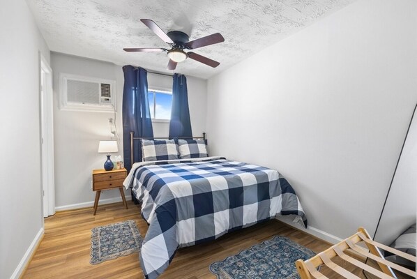 Une chambre à coucher avec un lit, un ventilateur de plafond, une table de chevet avec une lampe et une fenêtre avec des rideaux.
