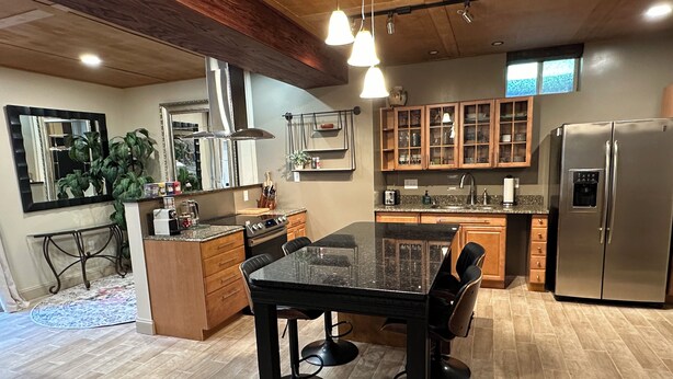 A modern kitchen with a central island, wooden cabinets, stainless steel appliances, and pendant lighting.