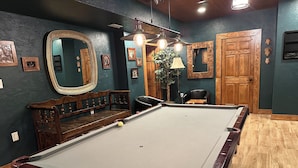 A pool table in a room with dark walls, wooden furniture, and framed pictures.