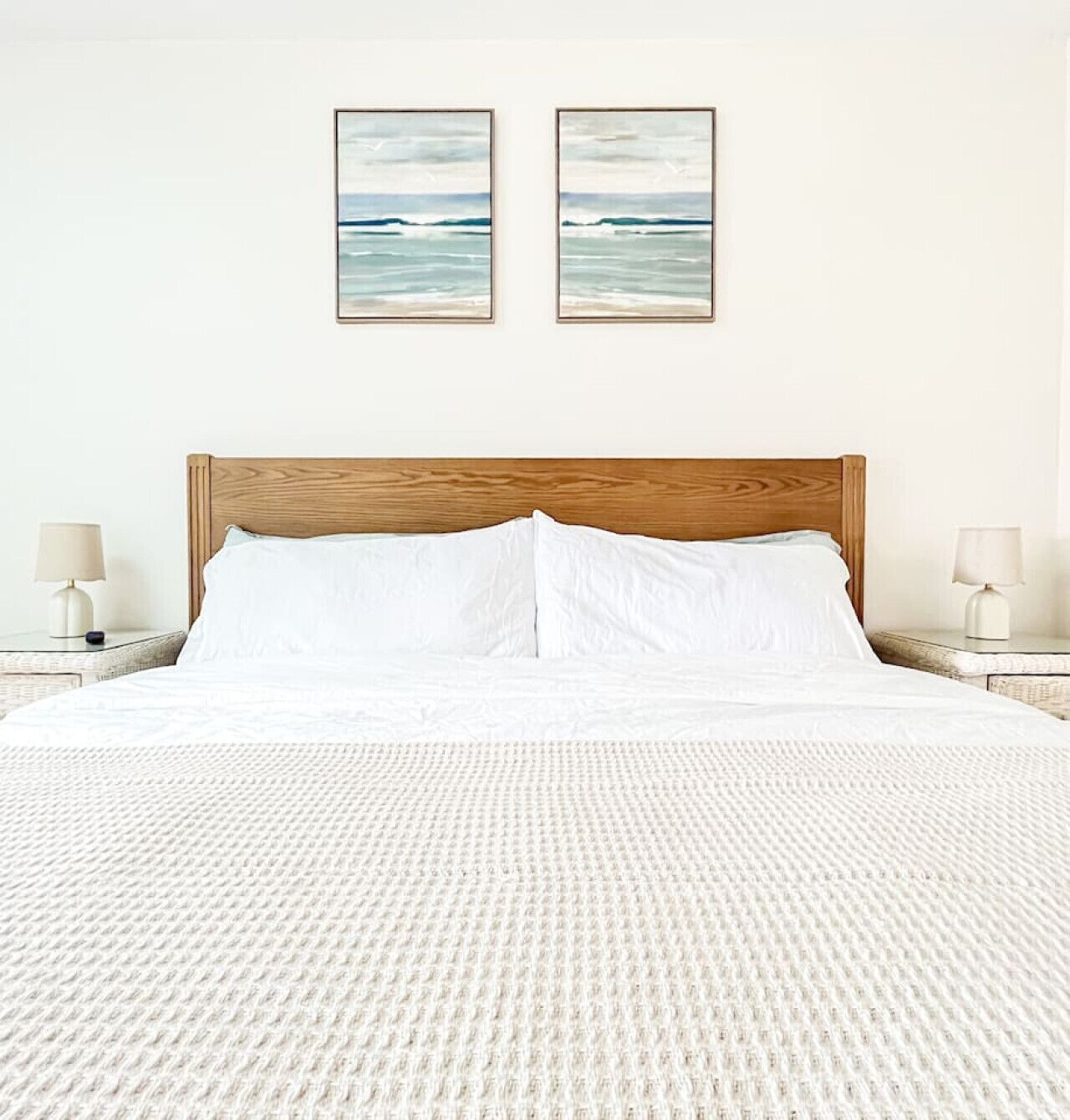 A bed with a wooden headboard, white bedding, and two framed pictures on the wall.