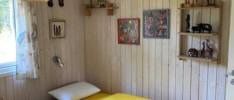 Een kamer met een bed, een bureau, een raam met gordijnen, een hanglamp en wanddecoraties, waaronder beeldjes van dieren en ingelijste foto's.