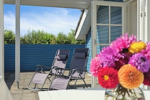 Une terrasse couverte avec deux chaises longues, une table blanche et un vase de fleurs.