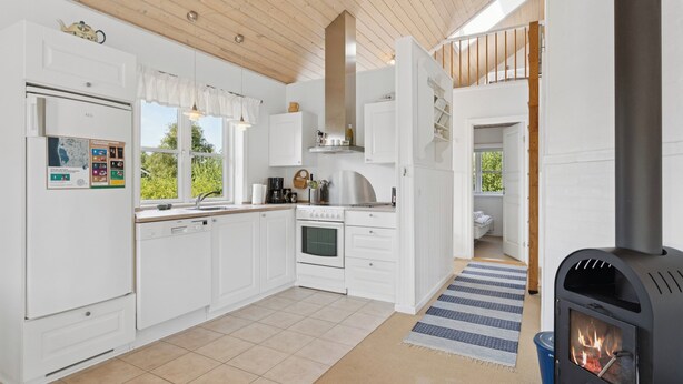 A modern kitchen with white cabinetry, a built-in oven, a stove, and a window overlooking greenery. - Peaceful cottage in scenic surroundings (Tarm)