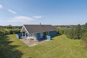 Ein eingeschossiges Haus mit Ziegeldach, einer überdachten Terrasse mit Gartenmöbeln und einem gepflegten Rasen.