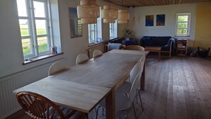 Zona de dinar amb taula i cadires de fusta, un sofà i una finestra amb vista a vegetació.