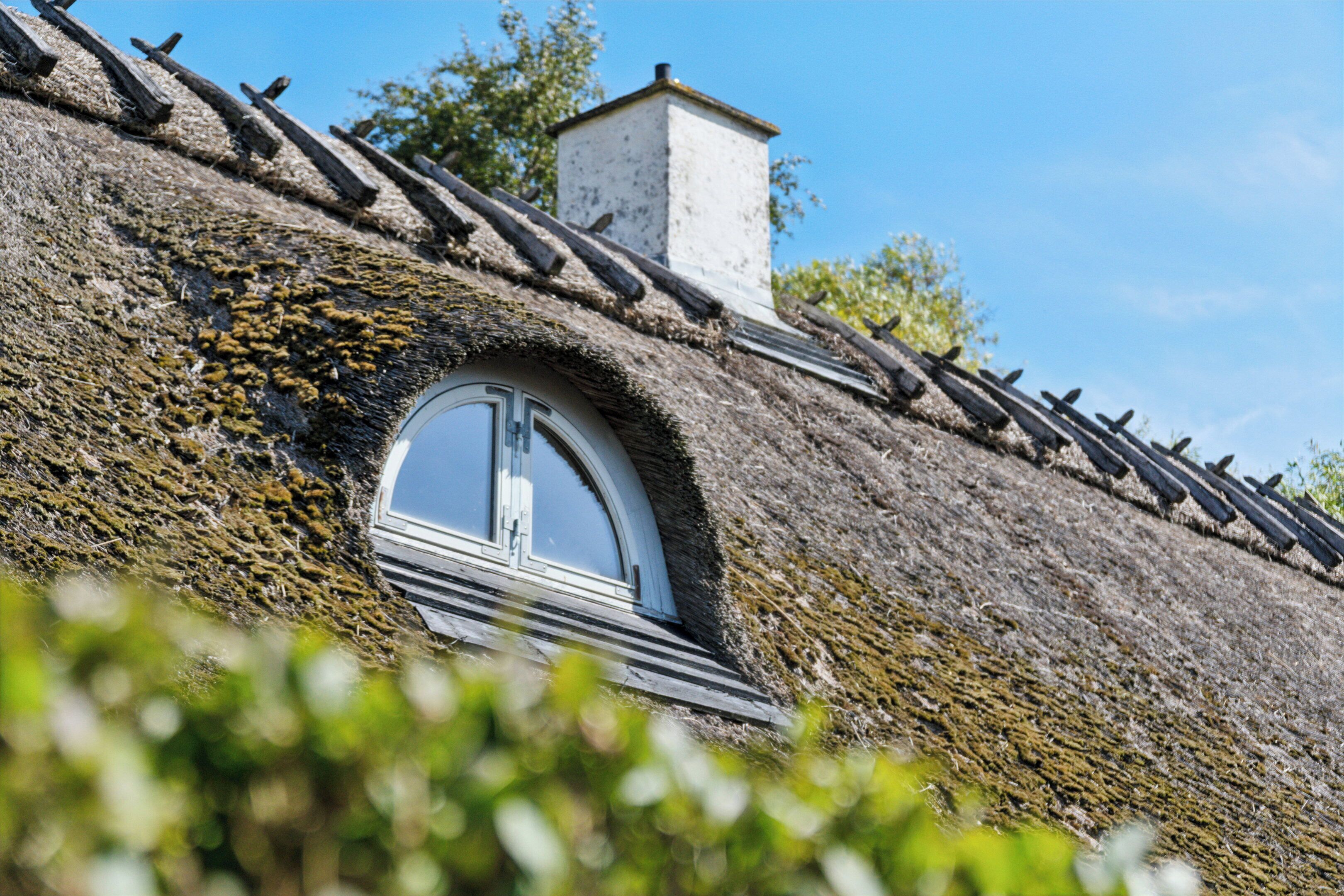 A rustic building with a thatched roof, a chimney, and a circular window.