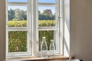 A window with two clear glass bottles on the sill, a white window frame, and a view of greenery outside.
