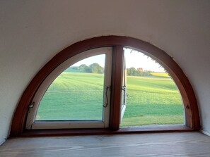 A room with a large arched window overlooking a green field.
