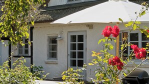 Una casa amb façana blanca, teulada de palla i un para-sol blanc.