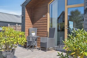 Eine Außenwand aus Holz mit der Nummer 92, eine Glastür und eine Terrasse mit Korbmöbeln und Blumentöpfen.