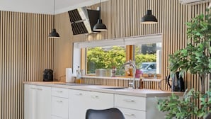 A modern kitchen with a large window, white cabinetry, and black pendant lights.