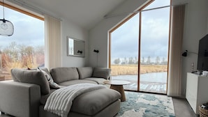 A modern living room with a sectional sofa, a round coffee table, and a large window offering a view of a field.