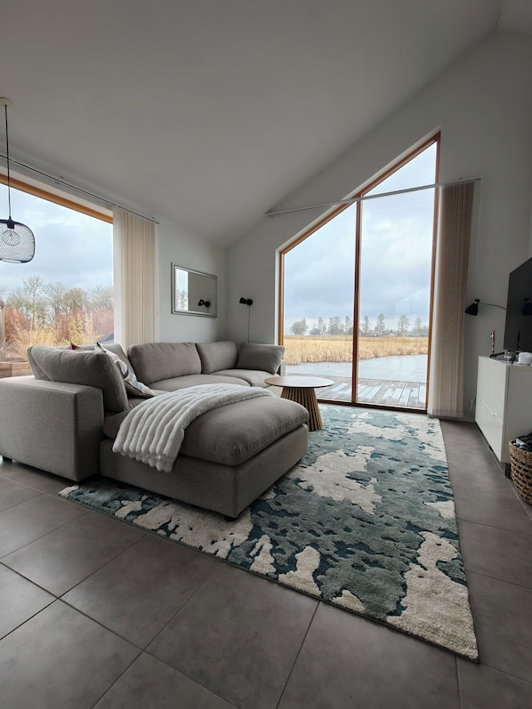 Ein modernes Wohnzimmer mit einer Eckcouch, einem runden Couchtisch und einem großen Fenster mit Blick auf ein Feld.