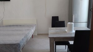Ein Schlafzimmer mit einem Bett, einem kleinen Tisch mit Stuhl, einer Toilette und einem Kühlschrank.