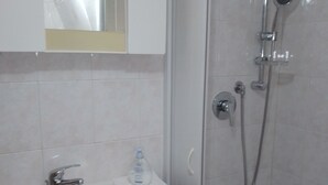 Ein Badezimmer mit einem weißen Waschbecken, einem Spiegel darüber und einer Duschkabine mit Handbrause und Wandarmatur.