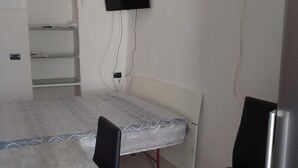 Ein Zimmer mit einem großen Tisch, zwei Stühlen, einem flachbildfernseher an der Wand und einem Kühlschrank.