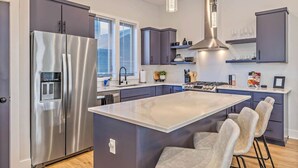 A modern kitchen with a stainless steel refrigerator, a central island with bar stools, and a built-in stove.
