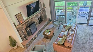 A living room with a stone fireplace, a flat-screen TV, a sofa, and a coffee table. - Mountain View Retreat ~Deck +grill! ~Jacuzzi Tub! (Flagstaff)
