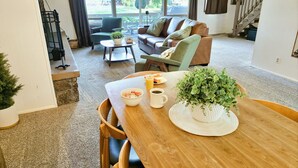 A cozy living room with a wooden dining table, a sofa, and a staircase. - Mountain View Retreat ~Deck +grill! ~Jacuzzi Tub! (Flagstaff)