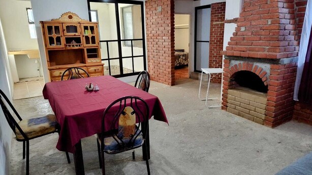 A dining area with a table set for two, a brick fireplace, and a wooden cabinet. - Comfortable and cozy apartment (Oaxaca de Juárez)