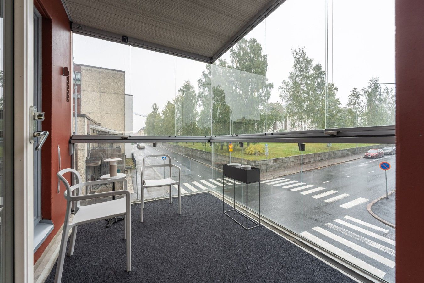 A room with a large window overlooking a street. There are two chairs and a small table.