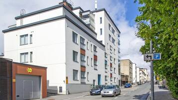 Un immeuble résidentiel à plusieurs étages, doté d’une architecture moderne, avec une porte de garage et un panneau indiquant un espace de stationnement à proximité.