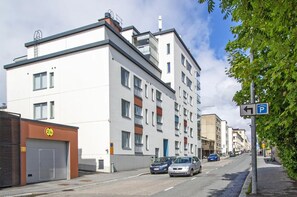 Un immeuble résidentiel à plusieurs étages, doté d’une architecture moderne, avec une porte de garage et un panneau indiquant un espace de stationnement à proximité.