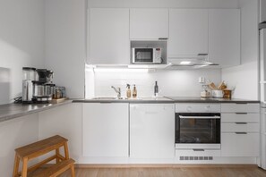 Une cuisine moderne avec des meubles blancs, un four à micro-ondes encastré, une machine à café, un évier et un four.