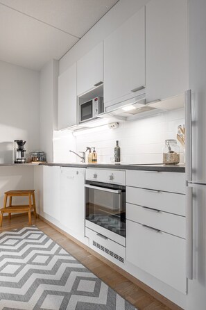 A modern kitchen with white cabinetry, a built-in oven, a microwave, and a coffee maker.
