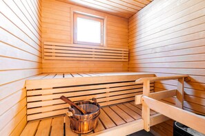 Un sauna avec des bancs en bois, une petite fenêtre et un seau en bois avec une louche.