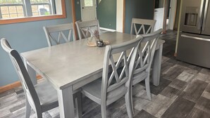 Un comedor con mesa y sillas, una cocina con refrigerador, y una puerta que da a otra habitación.