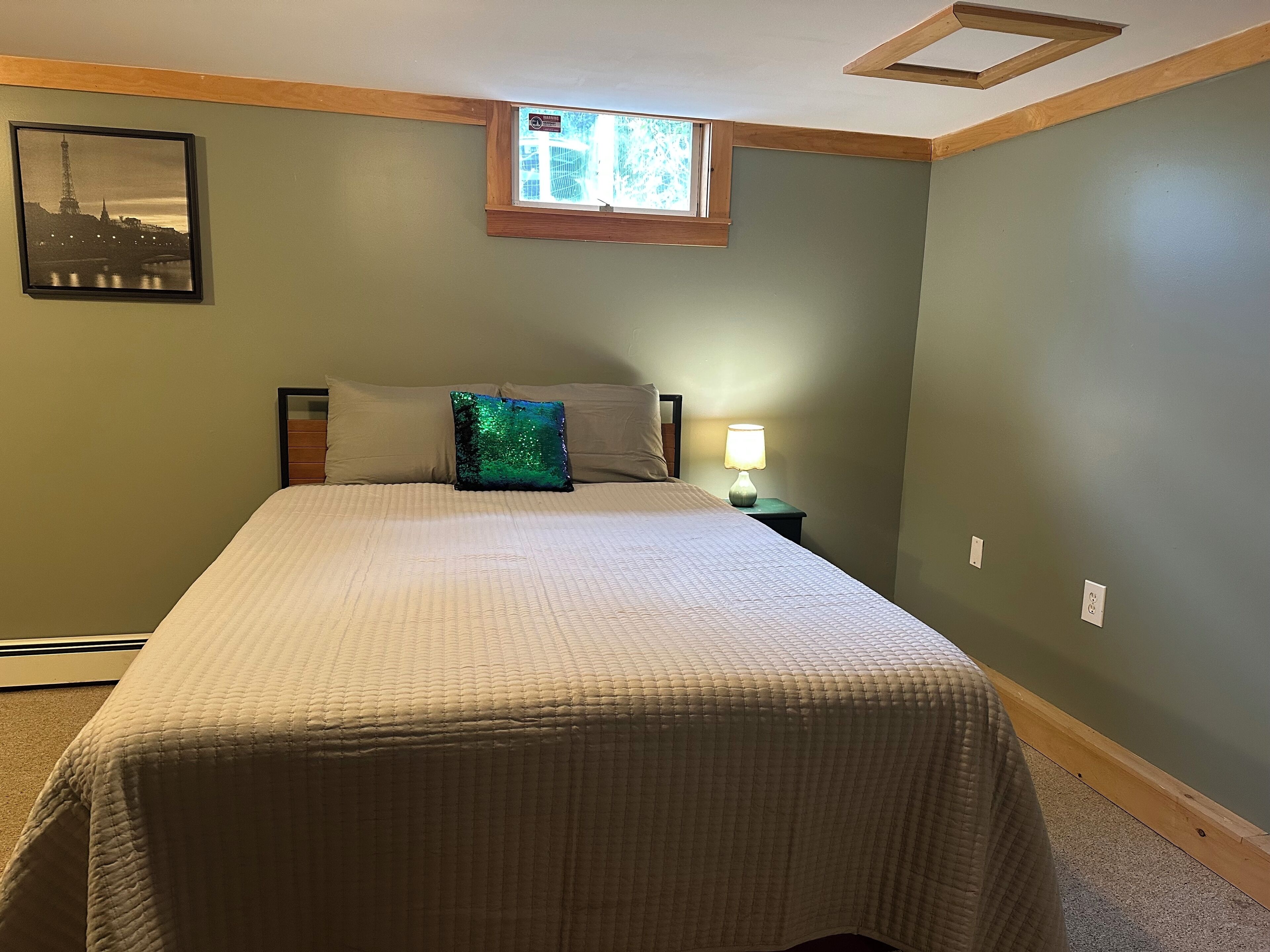 A bedroom with a bed, a nightstand, a lamp, a window, and a picture on the wall.