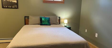 A bedroom with a bed, a nightstand, a lamp, a window, and a picture on the wall.
