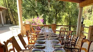 Un espace extérieur abrité, aménagé pour les repas, avec une longue table dressée et entouré de chaises en bois.