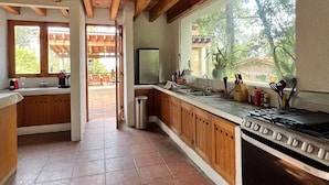 Une cuisine avec des poutres en bois, une cuisinière à gaz, un réfrigérateur et une fenêtre donnant sur un paysage verdoyant.