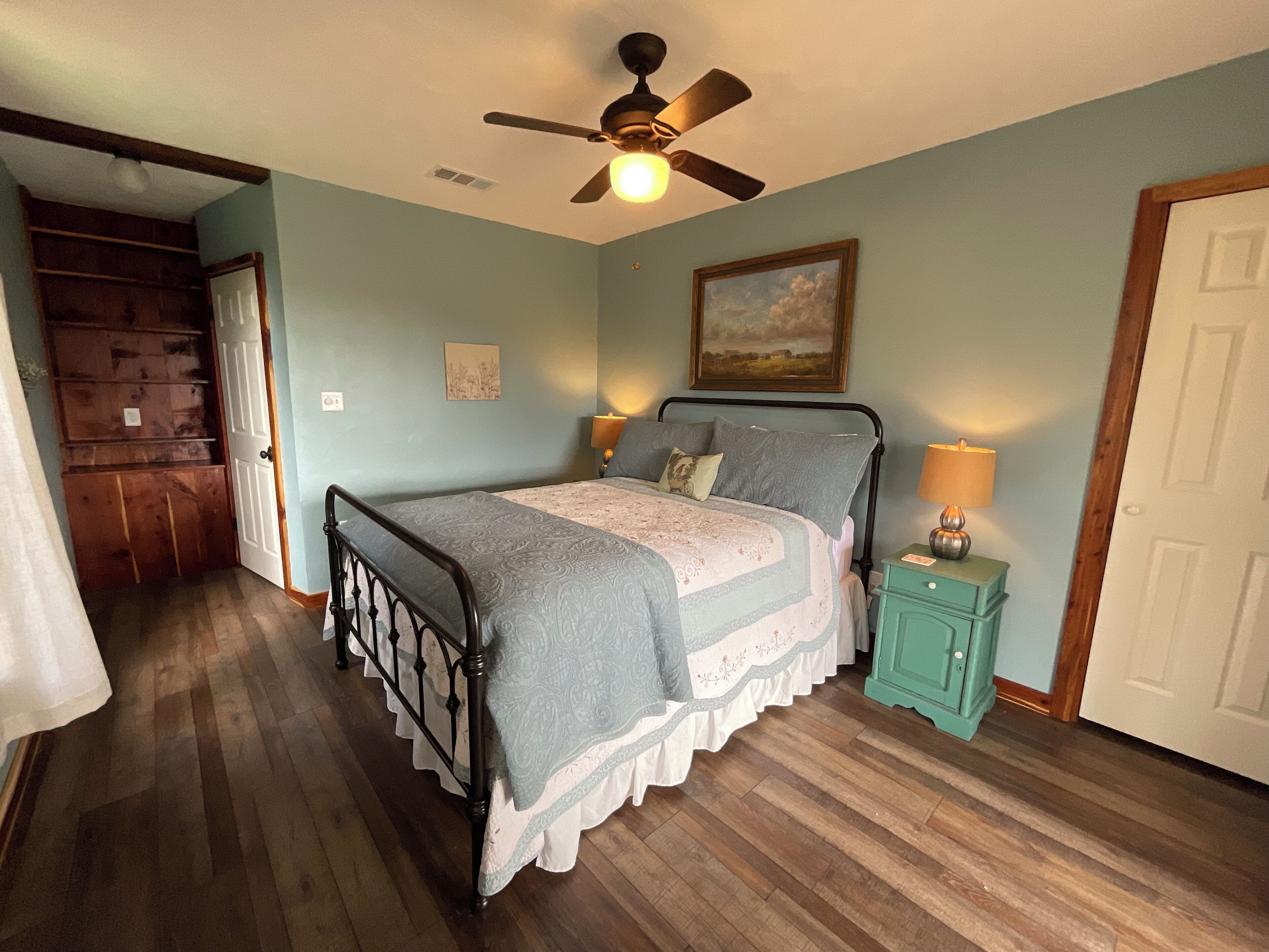 A bedroom with a bed, a ceiling fan, a nightstand, and a door.