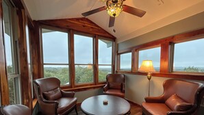 A room with a round table and four leather chairs, large windows with a view, and a ceiling fan.