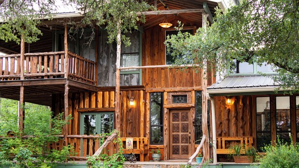 A rustic cabin with a wooden exterior, a balcony, and a front porch with steps leading to the entrance.