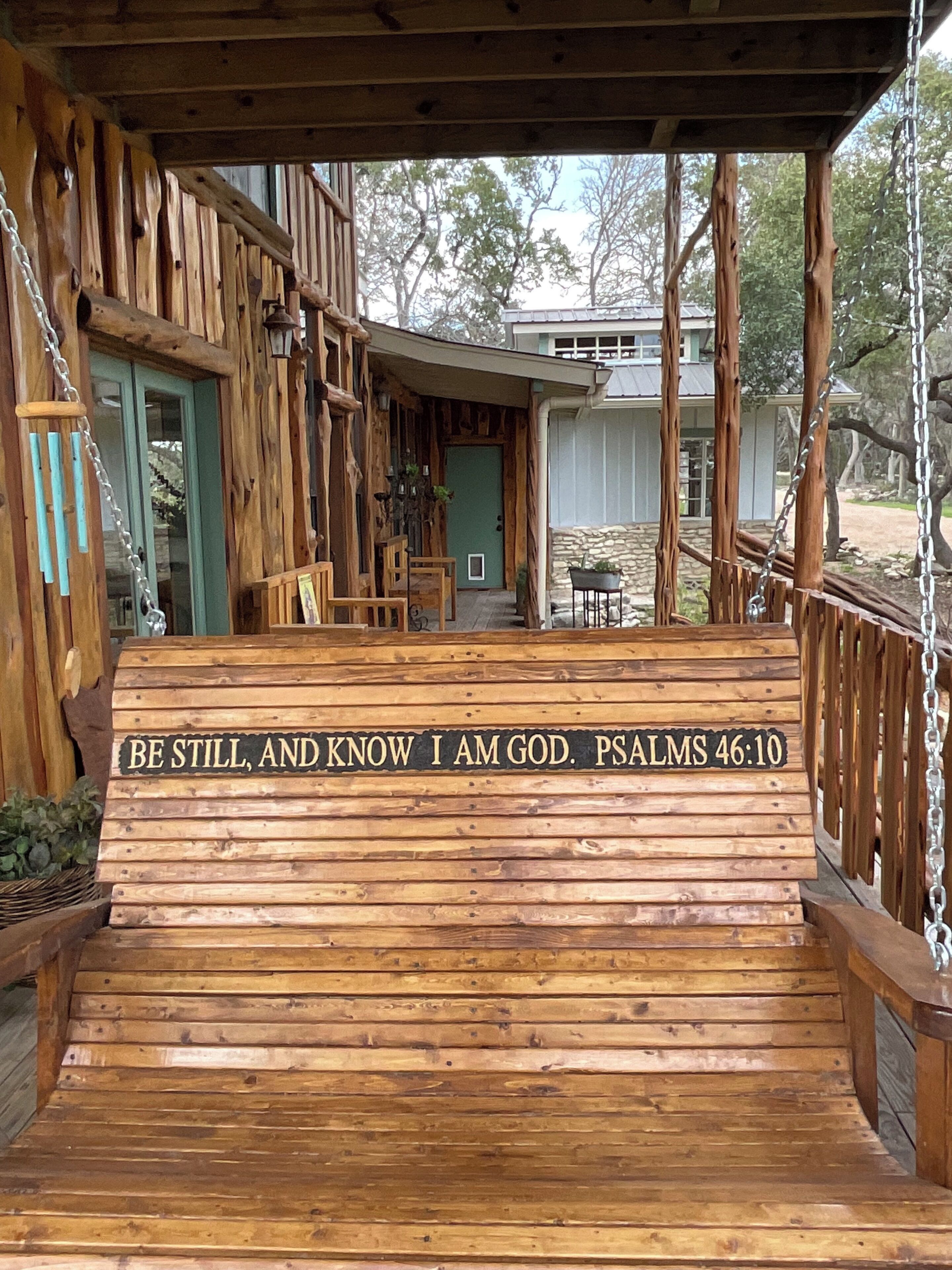 A wooden porch with a bench and a sign reading 'BE STILL, AND KNOW I AM GOD. PSALMS 46:10'.