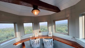 A room with a wooden bar, two white chairs, and large windows offering a view of the forest.
