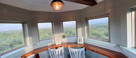 Una habitación con barra de madera, dos sillas blancas y ventanas amplias con vistas al bosque.