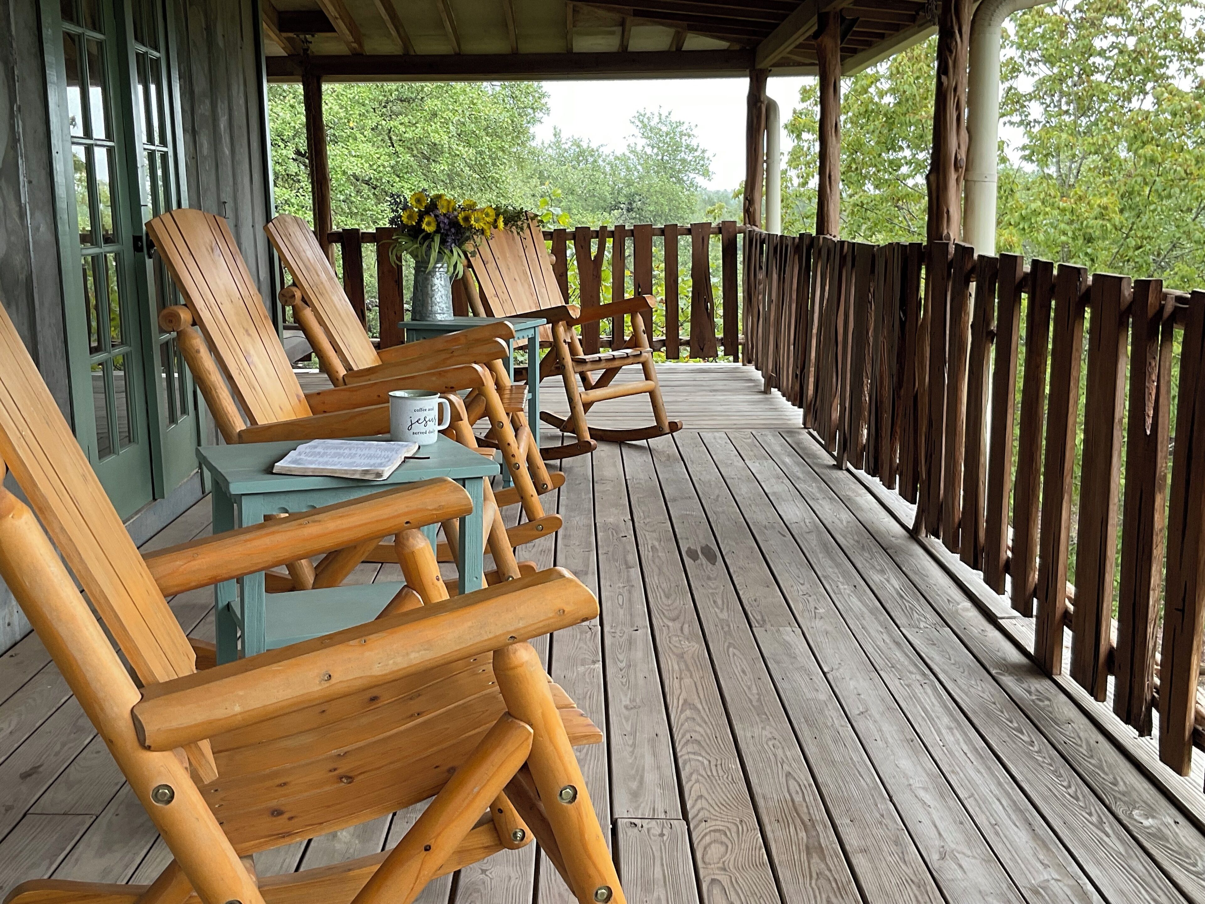 Een houten terras met buitenmeubilair, waaronder stoelen en tafels, en een uitzicht op groen in de verte.